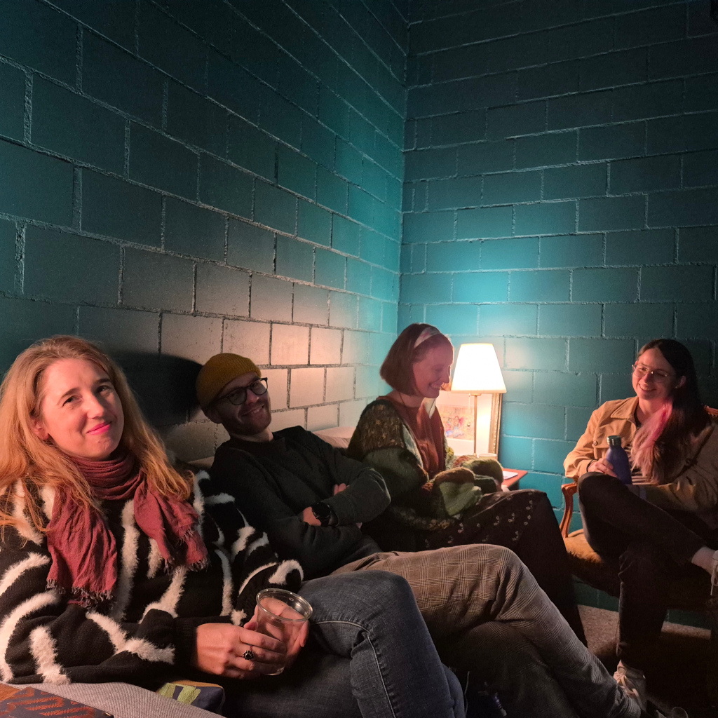 A photograph of four smiling people in a small green room.